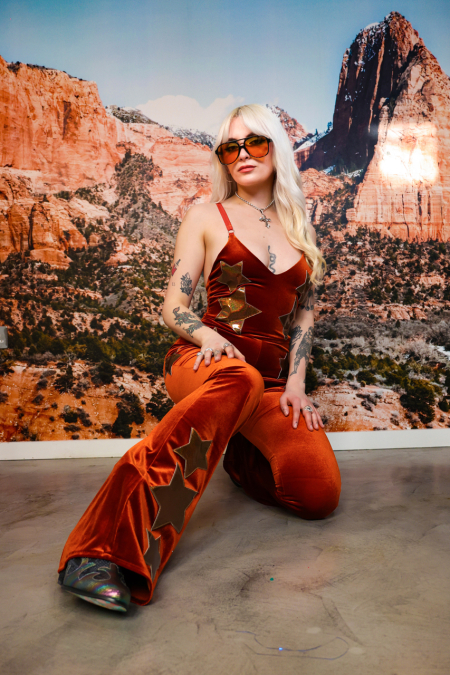 blonde woman in a burnt orange jumpsuit with gold stars