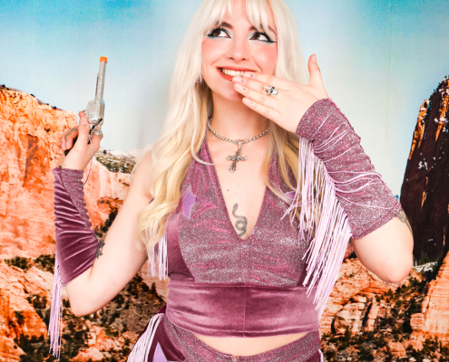 Blonde woman in a mauve western co-ord set holding a toy gun